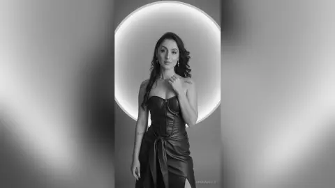 Elegant woman in a black strapless leather dress posing against a glowing circular light in a moody studio setting.