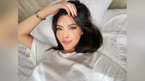 Beautiful woman with long dark hair wearing a white t-shirt relaxing on a white bed in a bright, cozy mood.