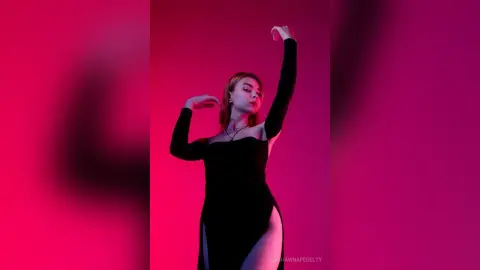 Elegant woman in a black long-sleeve dress posing against a vibrant pink studio background.