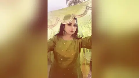 Elegant woman in a green traditional ethnic outfit posing gracefully under a sheer decorative fabric backdrop.