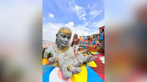 Woman in casual summer outfit standing by a giant stone hand sculpture under a blue sky in Medellin, Colombia.