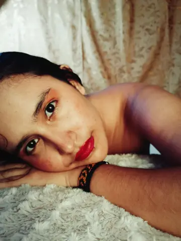 Young woman with red lipstick relaxing on a white shag rug in a cozy indoor setting.