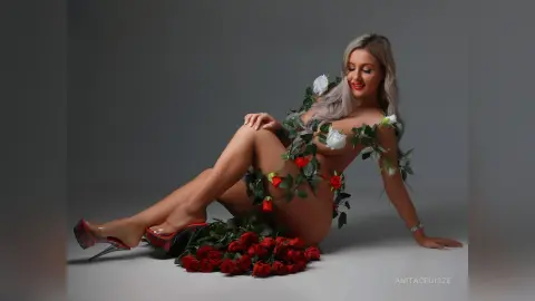Anita reclines on a grey floor, wearing a vine of white and red roses wrapped around her body.