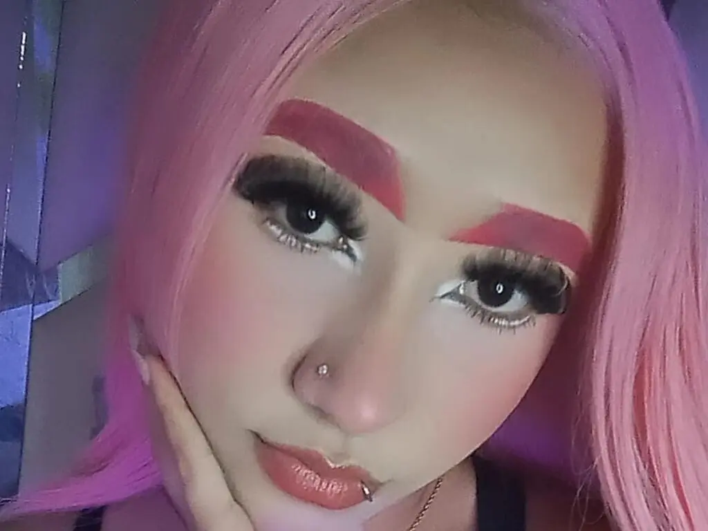 Close-up of a woman with pink hair, dramatic eyelashes, and bold makeup in a soft, dreamy mood.