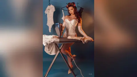 Glamorous woman in white vintage lingerie and gloves ironing lace clothing in a retro studio setting.