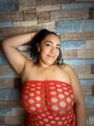 Smiling woman in a red polka dot strapless top posing against a rustic blue and brown wood plank wall.