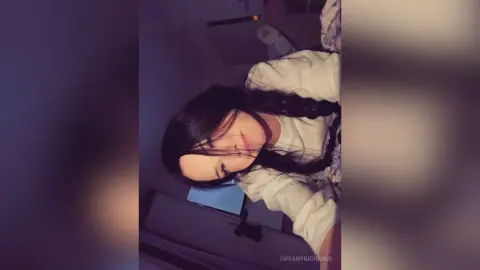 Young woman with long dark hair in a white shirt relaxing in a dimly lit room with a moody atmosphere.