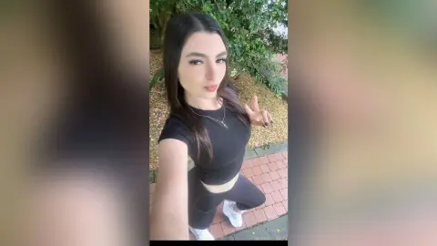 Young woman in black athletic outfit posing outdoors in a garden setting with a confident mood.