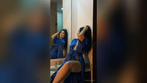 Elegant woman in a blue satin robe posing in a modern bathroom mirror with a moody, glamorous aesthetic.