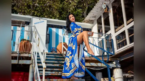MissyJolie poses outdoors on white stairs wearing a long blue and gold patterned open-front robe that shows her bare legs.