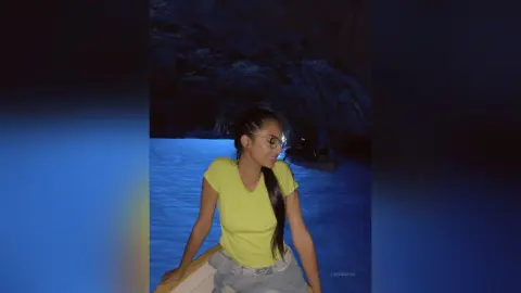 LucyMartin wears a yellow t-shirt and light denim jeans while standing outdoors at night near a body of water.