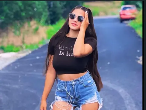 Young woman in black crop top and denim shorts posing on a sunny road with a relaxed summer vibe.