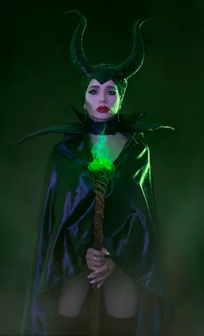 Mystical Maleficent cosplay featuring a dark horned headpiece and flowing black cape in a moody green fog.