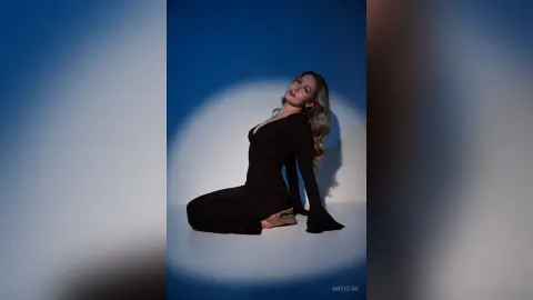 Elegant woman in a long-sleeve black dress posing against a blue studio background with dramatic lighting.