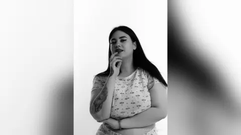 Portrait of a young woman in a patterned top posing with a thoughtful expression in a minimalist black and white setting.