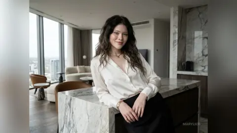 MaryLico leans against a white marble countertop wearing a white button-down shirt and a black skirt.