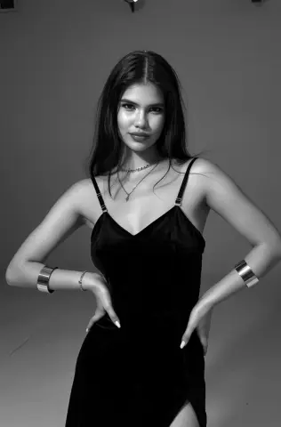 Elegant woman in a black velvet slip dress and silver jewelry posing in a minimalist studio setting.