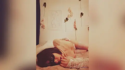 Woman in white lace lingerie lying on a bed in a minimalist bedroom with line art decor.