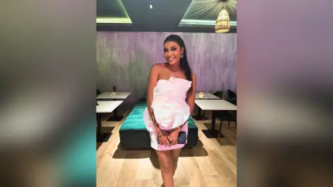Smiling woman in a white ruffled strapless dress posing in a modern, stylishly lit room.