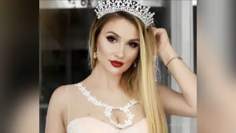 Elegant blonde woman in a white lace bridal gown wearing a silver tiara for a glamorous wedding portrait.