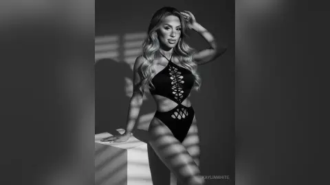 Elegant woman in a black cutout bodysuit posing in dramatic studio lighting for a moody black and white portrait.