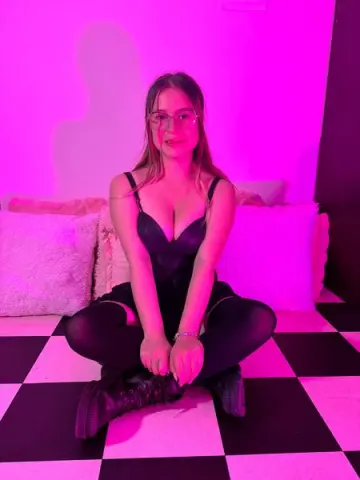Young woman in a black bodysuit sitting on a checkered floor under vibrant pink neon lighting.