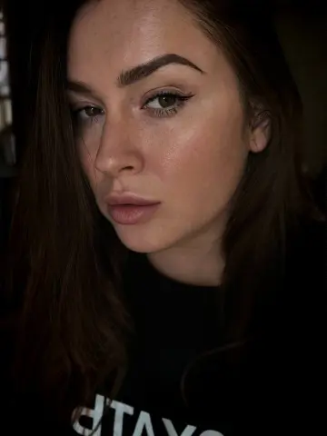 AliceOfWondersss looks directly at the camera with long brown hair and winged eyeliner, wearing a black top.