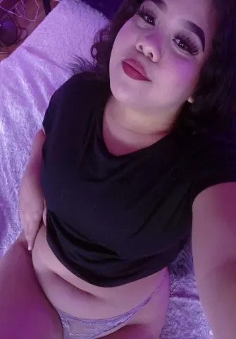Young woman in a black t-shirt and lace underwear relaxing on a soft white blanket with moody purple lighting.
