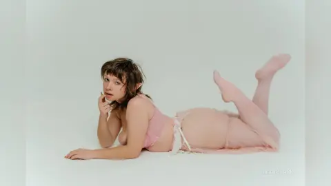 Young woman in pink lace lingerie lying on a white floor in a soft, dreamy aesthetic.