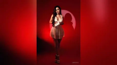 LaraCole poses in a white plunging neckline dress with long wavy hair against a red background.