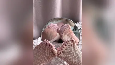 Close-up of feet in pink fishnet stockings resting on a soft white textured surface in a cozy indoor setting.