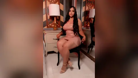 Elegant woman in a pink satin slip dress sitting in a stylishly lit room with a sophisticated mood.