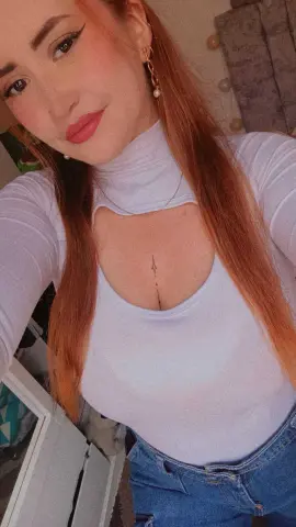 Redheaded woman in a white turtleneck top and blue jeans posing in a bright indoor setting.