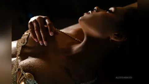 Elegant woman in a sparkling gold sequin gown posing gracefully in moody, dramatic low-light lighting.
