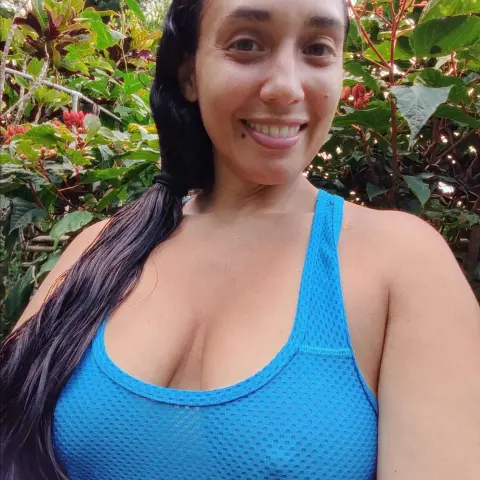 Smiling woman in a blue athletic tank top relaxing in a lush green garden setting.