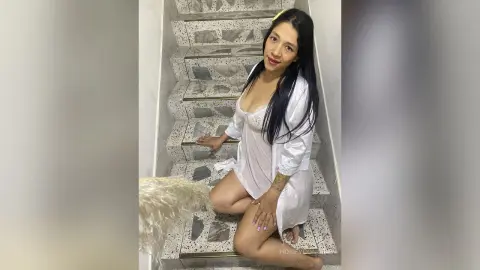 Young woman in a white silk robe sitting on marble stairs in a bright, modern indoor setting.