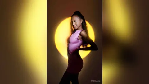 Young woman in a pink sleeveless top posing against a warm, glowing yellow circular light background.