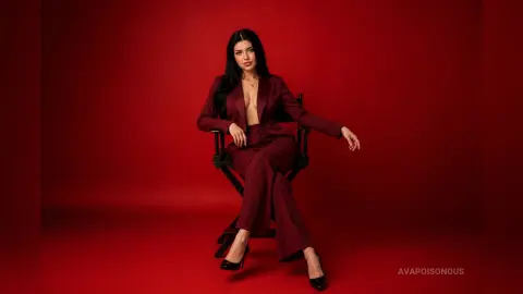 Elegant woman in a burgundy power suit sitting on a chair against a bold red studio background.