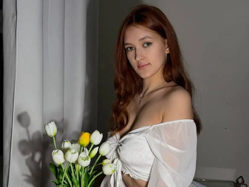 Young woman in a white off-the-shoulder top posing with white tulips in a bright, soft-lit indoor setting.