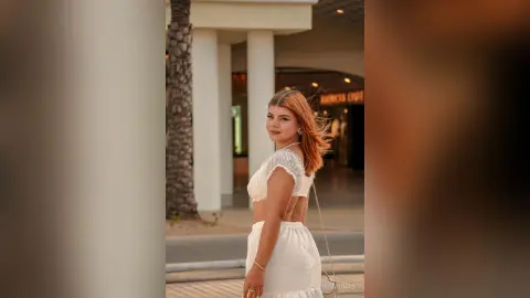 Young woman in a white summer outfit standing outdoors near a building during golden hour.