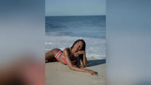 Relaxed woman in a red bikini lounging on a sunny beach with ocean waves in the background.
