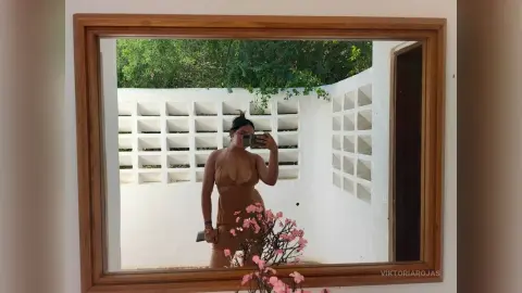 Woman in a brown swimsuit taking a selfie in a bright, minimalist white patio setting.