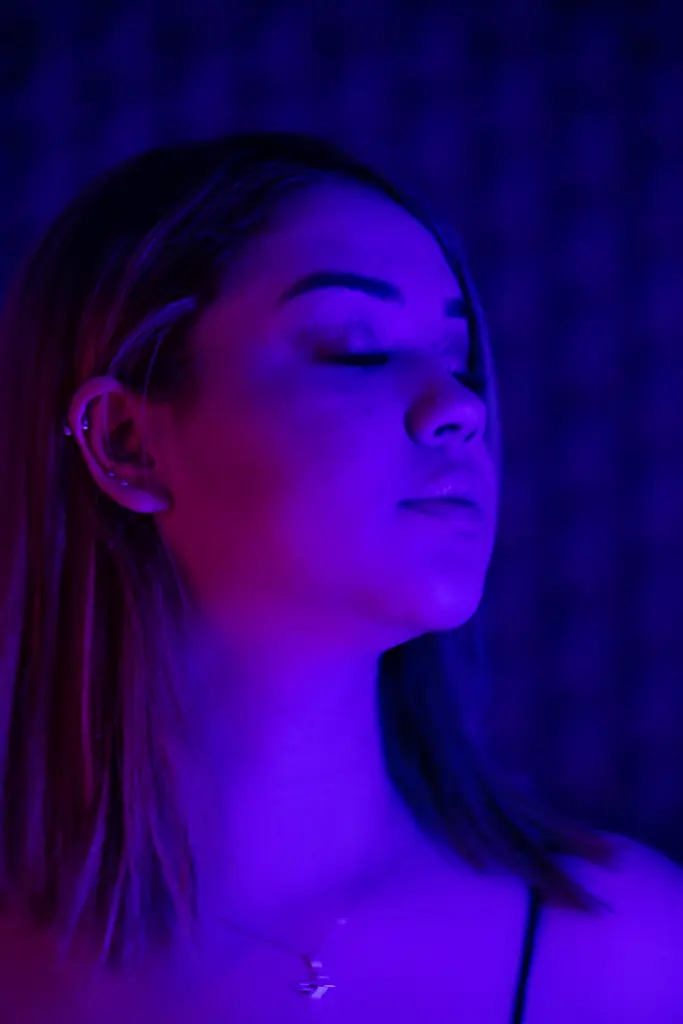 Amber_Duran — Young woman with closed eyes in moody blue and pink neon lighting.