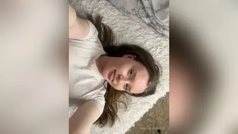 Young woman in a white t-shirt relaxing on a cozy white textured blanket in a bright, peaceful setting.