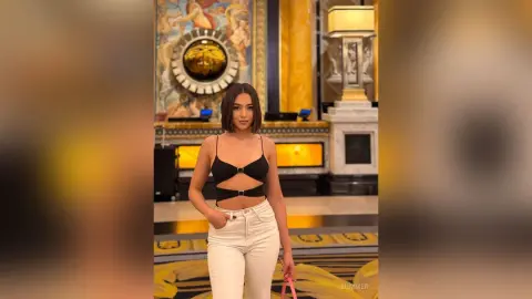 Stylish woman in a black crop top and white jeans posing in a luxurious golden hotel lobby.