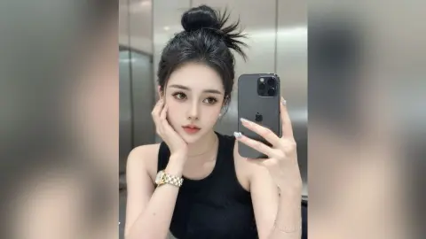 AgelaHui poses for a mirror selfie wearing a black tank top, with her dark hair styled in a high bun and a gold watch on her wrist.