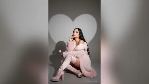 AnnyeWilliams poses in a pink fuzzy coat and matching boots while holding a pink lollipop against a heart-shaped shadow.