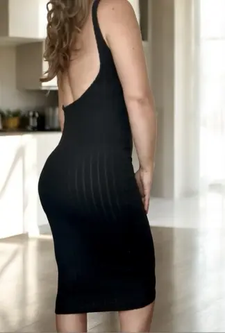 CurvyHannahXX poses in a tight black ribbed dress that shows off her curves and back in a bright room.