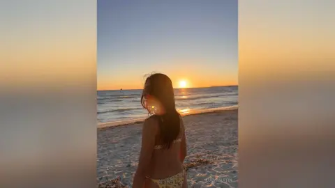 LucyMartin poses on a sandy beach at sunset, wearing a patterned bikini and looking back over her shoulder.