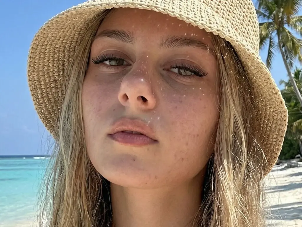 Close-up portrait of a blonde woman in a straw sun hat enjoying a sunny tropical beach vacation.